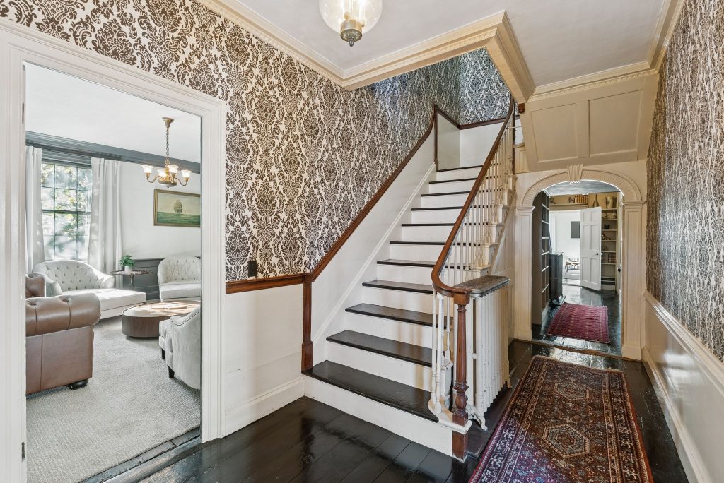 Historic Portland Maine inn entryway featuring an elegant Victorian staircase, original dark wood floors, ornate damask wallpaper, and classic architectural details, offering a timeless and refined guest experience.